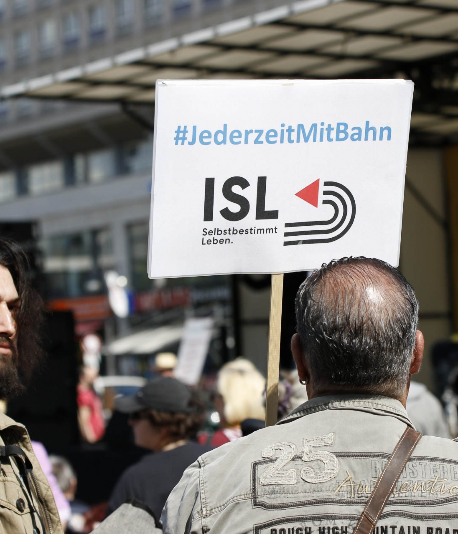 Mensch von hinten zeigt Schild mit ISL Logo bei einer Demonstration nach oben