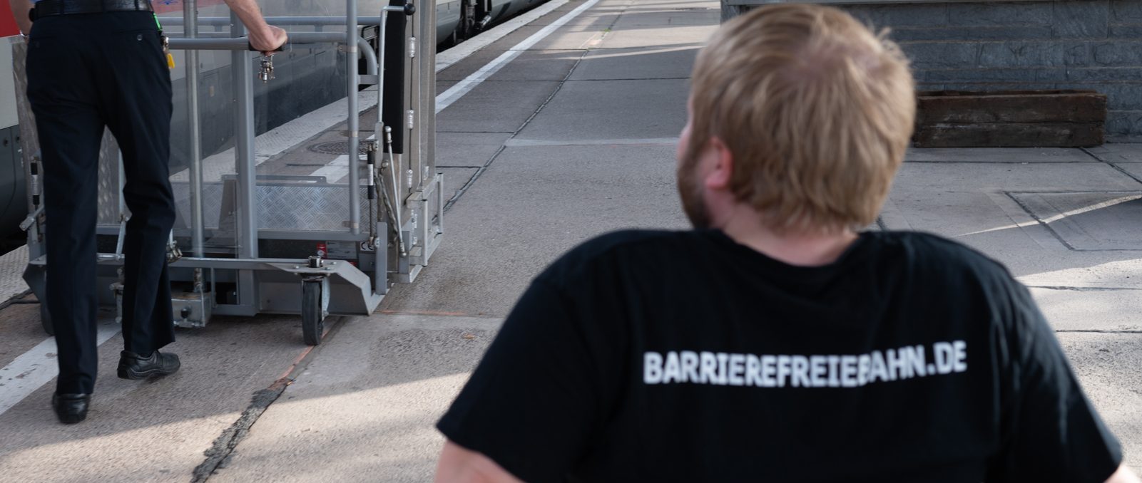 Mensch im Rollstuhl folgt Bahnmitarbeiter mit Hublift an einem Bahnsteig mit einem ICE Foto: Jacqueline Hirscher