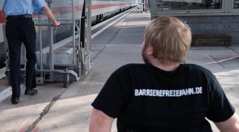 Mensch im Rollstuhl folgt Bahnmitarbeiter mit Hublift an einem Bahnsteig mit einem ICE Foto: Jacqueline Hirscher