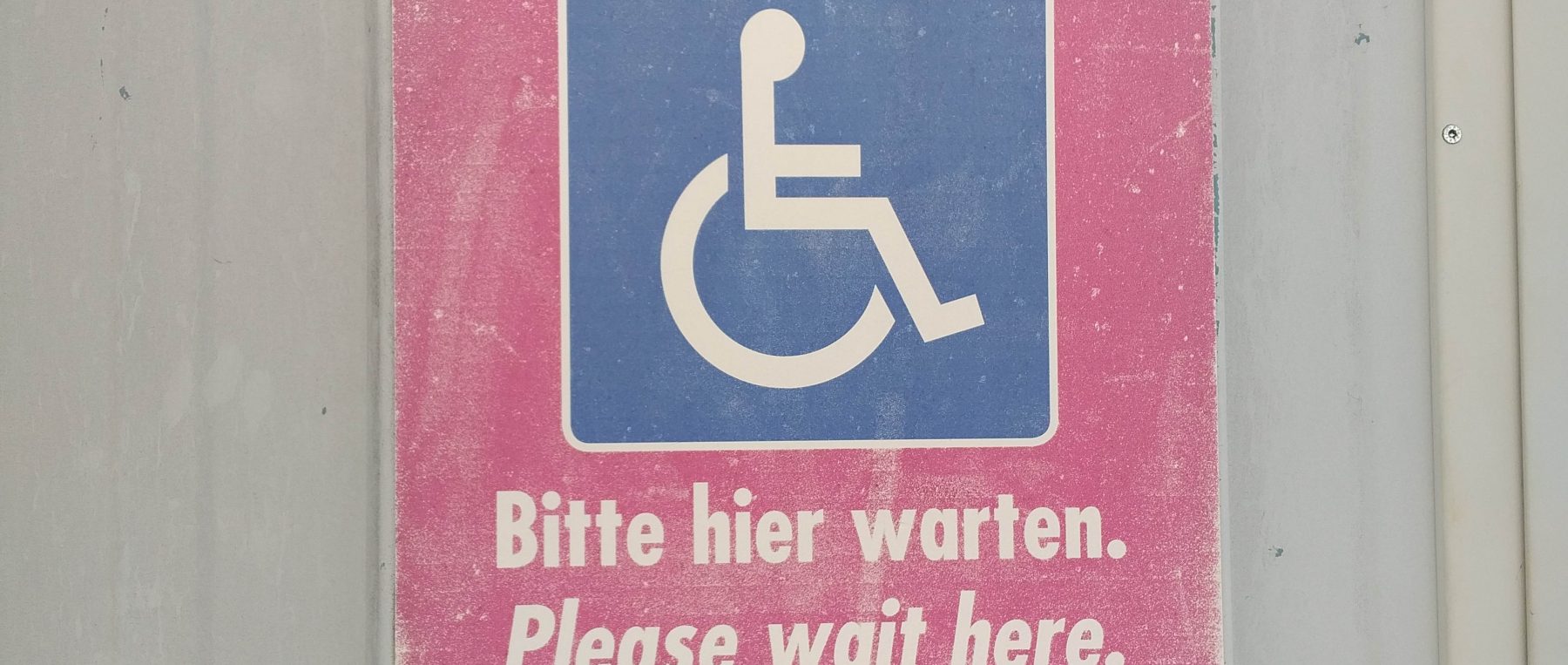 Rollstuhlsymbol mit Aufschrift Bitte hier warten Please wait here