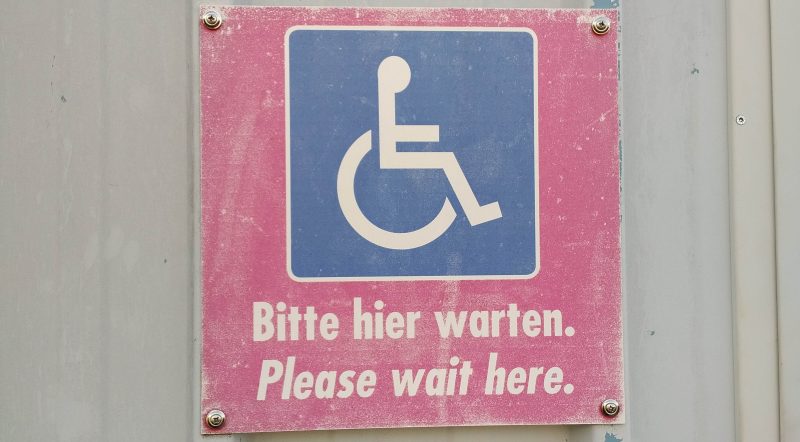 Rollstuhlsymbol mit Aufschrift Bitte hier warten Please wait here